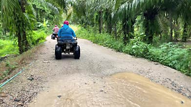 Group of tourists riding ATV quad bikes in convoy through Phuket Thailand jungle,