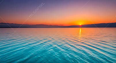 Vibrant sunset over calm turquoise water with distant mountains ocean lake