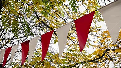 Red and white triangular bunting hanging against a background of bright yellow autumn foliage and sky
