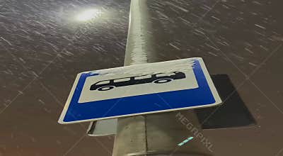 A bus stop sign is covered in fresh snow during a winter night. Heavy snowfall
