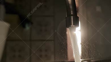 Water splashing from a bathroom tap against the backdrop of the sunset, slow motion, industry. Copy space for text