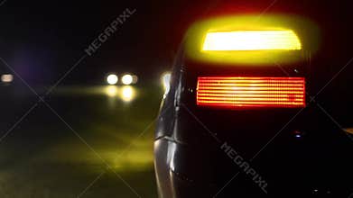 Flashing orange blinker light on sport car parked on side at night.