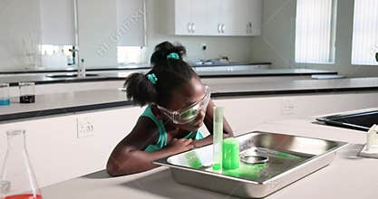 Kid is pouring green liquid into cylinder after placing beaker in tray on bench observing reaction