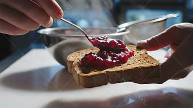 Hands Spreading Homemade Berry Jam on Sliced Toast Close-up Food Prep on White Surface with Natural Lighting in Kitchen Setting