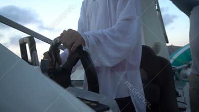 Boat driver steering wheel sailing a motorboat on the ocean at dusk wearing white casual clothes travel adventure