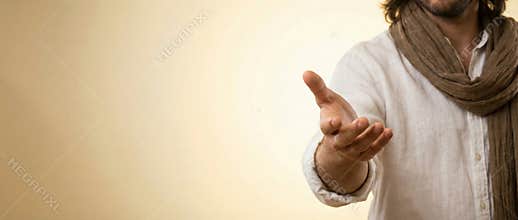 Man with long hair and a scarf, dressed in plain white clothing, extending an open hand in a welcoming and inviting gesture