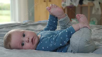 Playful baby exploring toes on bed