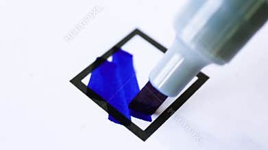 Hand coloring a square checkbox with a blue marker on paper, symbolizing selection, decision-making, or voting action, close-up