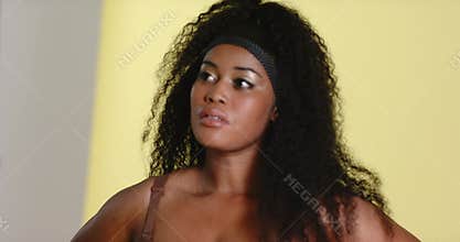 After cue, African American woman turning head, tucking hair, posing confidently on yellow backdrop