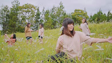 Young woman smiling and playing with wild grass with friends behind her