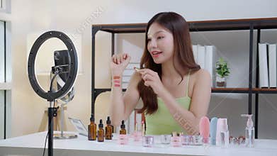 Young asian beauty influencer testing multiple lipstick shades on arm while recording makeup review at home, cosmetic product of