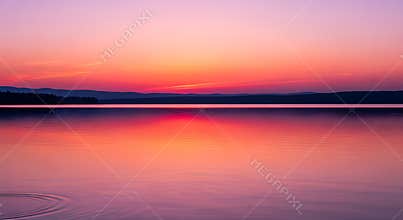 Pink and orange sunset over calm lake with distant hills water