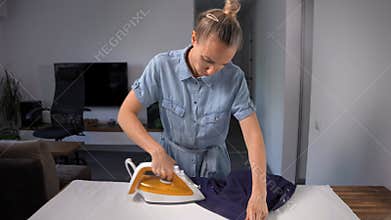 Middle-aged woman ironing a man's shirt in her living room. Domestic chore.