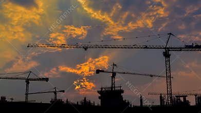 Time lapse sunset and silhouette crane working in big construction site (zoom out)