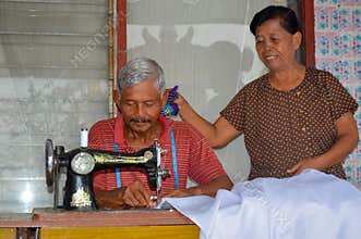 Elderly Wife Wiping Husband's Sweat While He Sews