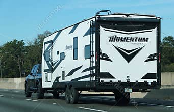 Lakeland, Florida, U.S.A - Jan 2, 2026 - A black and white Momentum Grand Design travel trailer towed by pickup truck, featuring