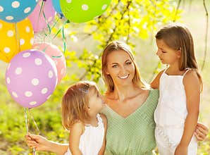 Happy woman and her little daughters in the park with ballons