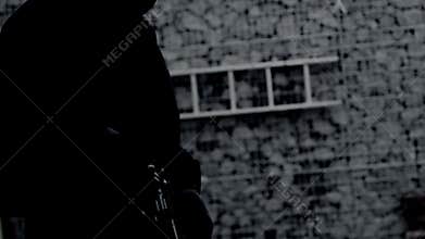 unrecognizable killer, bandit, or man in a hood and mask leaning against a wall, in ambush, reloading a pistol magazine