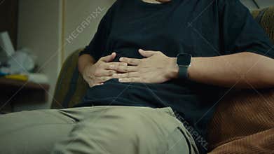 Slow motion of person massaging abdomen for discomfort while seated