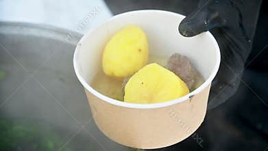 We pour a cup of delicious fresh soup with potatoes, vegetables, and meat from a cast-iron pot. Close-up of the soup contents.
