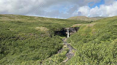 Expansive Green Meadow with Tiny Waterfall and Rocky Stream in Iceland