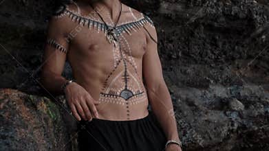 Handsome and courageous European man with drawings on his body stands at a cliff