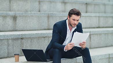 Businessman reading business papers on street. Man sitting on stairs