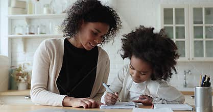 Afro american mom helping cute school child daughter checking homework