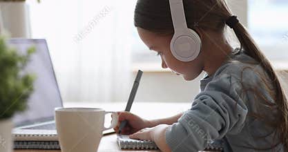Pretty primary school girl wearing headphones distance learning at home