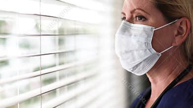Stressed Doctor or Nurse On Break At Window Removing PPE, Face Mask and Protective Glasses