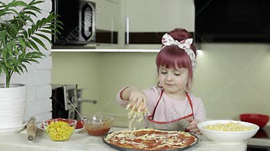 Cooking pizza. Little child in apron adding grated cheese to dough in kitchen