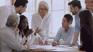 Confident middle aged female boss holding brainstorming meeting with executives.
