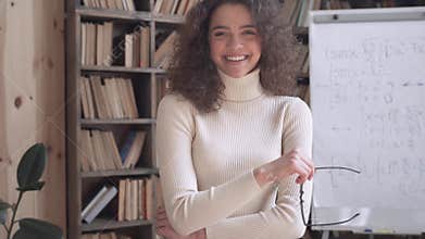 Smiling latin lady teacher looking at camera laughing in classroom, portrait.