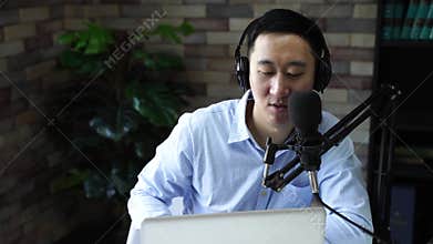 Young adult businessman podcasting and recording talk show at home studio with computer laptop on table. The desk is