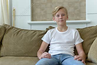 Young handsome boy with blond hair sitting on the sofa