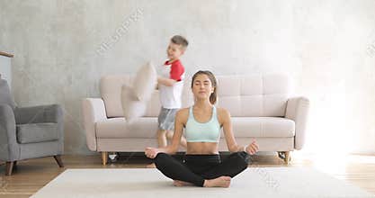 Woman mom is meditating at home and her son running aroung her trying to play.