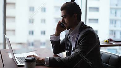 Side view of successful young businessman doctor in business suit with stethoscope typing on laptop