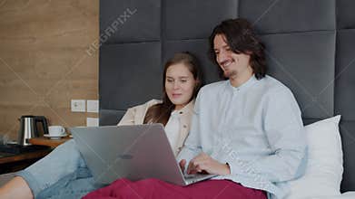 Man and woman using laptop computer and talking in bed in hotel room