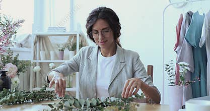 Young female designer arranging green floral branches in composition.