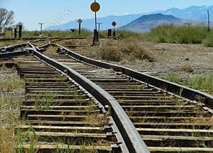 Narrow gauge railroad tracks run toward a switch junction and signals in an old train yard
