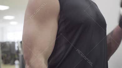 Close-up of muscular hand of Caucasian sportsman lifting hand weights in gym. Unrecognizable man raising dumbbells for