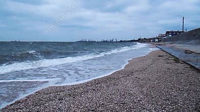 Storm at sea with big waves. Sandy shore. Side view of the coastline and the seaport. HD video