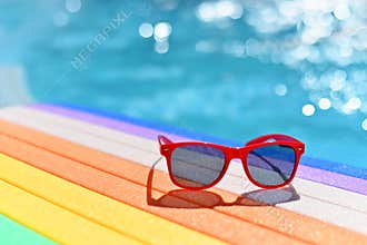 Summer background. Concept for summer and vacation. Red sunglasses by the pool in the background with blue water