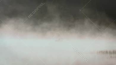 Silhouette of a fisherman on a boat in the morning mist on the lake