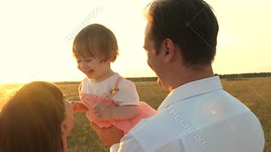 Dad and mom playing with a little daughter in her arms at sunset. family walks with a child at sunset. father playing