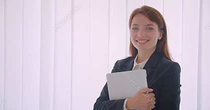 Closeup portrait of young caucasian businesswoman holding the laptop looking at camera smiling happily standing indoors