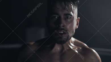 Angry man with boxing gloves screams emotionally looking ar the camera standing on the boxing ring. Slow motion.