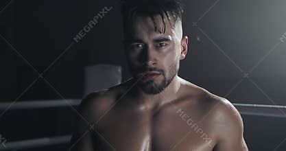 Portrait of angry male boxer standing on the boxing ring and looking intensely at the camera.