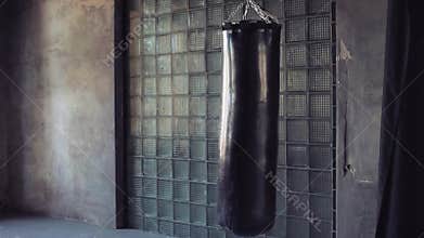 Dark grunge gym, punching bag swinging from the kick, nobody.