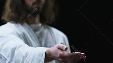 Jesus Christ reaching out his hand against dark background, helping people